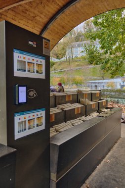 Bu görüntü, Lourdes Hanımefendisi 'nin Sığınağı' nda bir mum otomatının açık havada dokunmatik bir ödeme sistemiyle mum sunuşunu gösteriyor. Bu ikonik hac ziyaretinde bir anlık dini bağlılık ve turizm sahnesini yakalıyor.