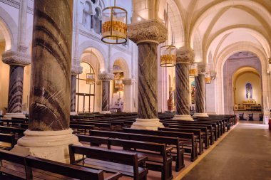 Lourdes France 'ın Kutsal Yürek Kilisesi' nin iç manzarasında mermer sütunlar, kemer sıraları ve asılı ışıklar gibi mimari ayrıntılar sergilenmektedir. Bu resim seyahat turizmi, dini ve mimari amaçlar için kullanılabilir..