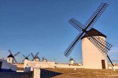 La Mancha İspanya 'daki Don Kişot yel değirmenlerinin Campo de Criptana köyündeki geleneksel beyaz yel değirmenlerini açık mavi gökyüzü altında sergilediği manzara. Bu görüntü turizm ve kültür projeleri için mükemmel..