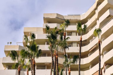 Benalmadena mimarisinin dış görünüşü ile Costa del Sol İspanya 'da palmiye ağaçları modern bina tasarımı ve balkonlarını bulutlu bir gökyüzü altında sergiliyor. Bu resim seyahat ve turizmle ilgili içerik için uygundur.