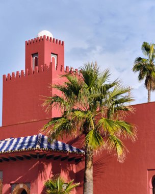 Palmiye ağaçlı kırmızı bozkır kalesi El Bil Bil İspanya 'nın Benalmadena Costa del Sol şehrinde berrak bir mavi gökyüzüne karşı bu popüler seyahat noktasının eşsiz mimarisini ve tropikal atmosferini sergiliyor..