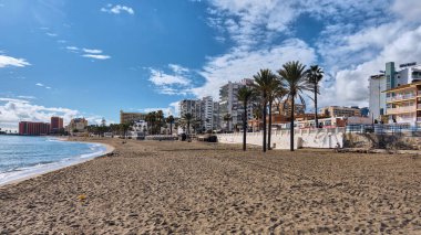 Benalmadena, İspanya - 24 Aralık 2025: Panoramik bir manzara sahilin kumlu kıyılarını kaplayan palmiyeleri, mavi denizi ve kıyı binalarını, güneşli bir gökyüzünün altında Costa del Sol İspanya 'da tipik bir manzara sunar..