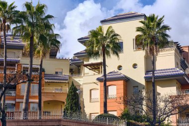 Benalmadena Costa del Sol İspanya 'da palmiye ağaçlı apartman manzarası, bulutlu bir havada Akdeniz mimarisi ve mavi kiremitli çatılar sergiliyor.