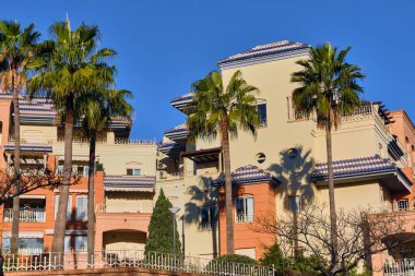 Benalmadena Costa del Sol İspanya 'da palmiye ağaçlı apartman manzarası, bulutlu bir havada Akdeniz mimarisi ve mavi kiremitli çatılar sergiliyor.