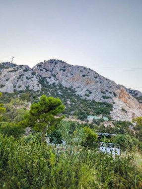 Wild Mediterranean vegetation and shrubs grow beneath towering rocky mountain peaks near Antalya Turkey under clear sky. High quality photograph