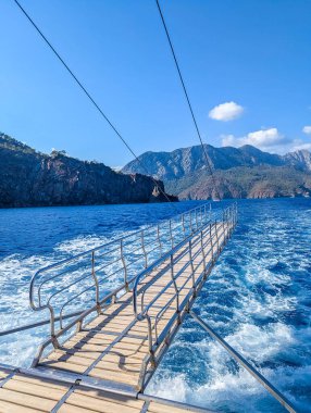 Dramatic view from boat deck shows Mediterranean Sea wake with mountain coastline and clear blue sky near Antalya Turkey. High quality photograph