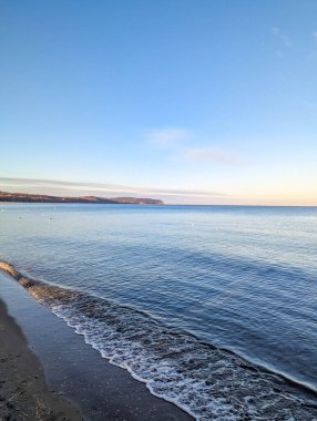 Gentle wave creates delicate foam pattern on Baltic Sea shore with smooth water surface under overcast sky in Sopot Poland. High quality photograph
