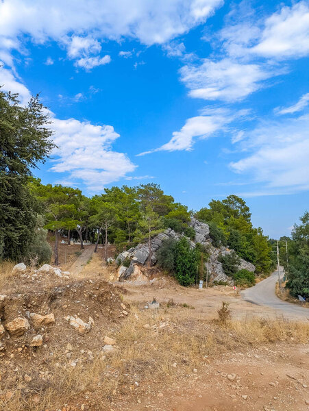 Dry Mediterranean terrain with green trees and shrubs spreads beneath mountain range under scattered clouds near Antalya Turkey in summer. High quality photograph