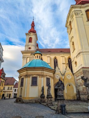 Zatec, Çek Cumhuriyeti, 1 Mayıs 2025. Zatec Çek Cumhuriyeti şehir meydanında yeşil kubbeli ve tarihi çeşme heykeli olan Barok kilisesi. Yüksek kalite fotoğraf