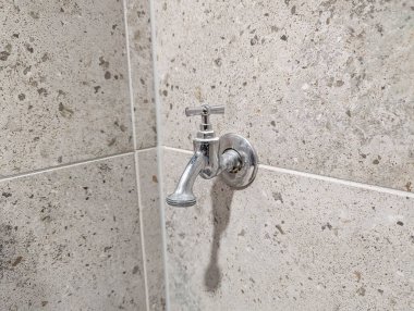 Chrome water shut off valve mounted on speckled beige concrete bathroom wall with visible plumbing fixture. High quality photograph.