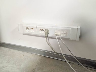 Minimalist açık gri duvar yüzeyine bağlı fiş kablosu olan beyaz elektrik prizi. Yüksek kalite fotoğraf.