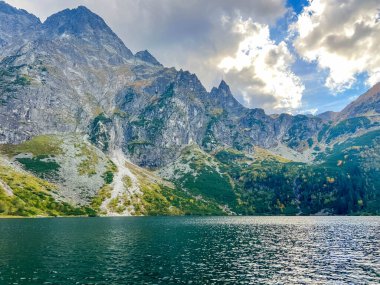 Zakopane Polonya 'nın vahşi doğasında bulutlu gökyüzü ile sakin alp gölü üzerinde yükselen dramatik kayalık Tatra dağ zirveleri. Yüksek kalite fotoğraf.