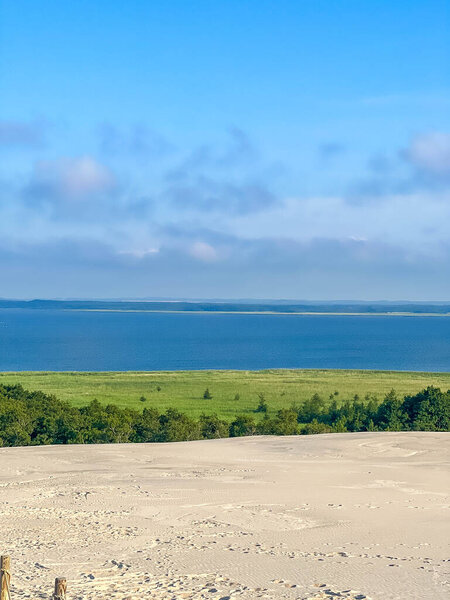 Elevated view of moving Baltic Sea sand dunes with green forest coastline and blue water in Leba Poland. High quality photograph