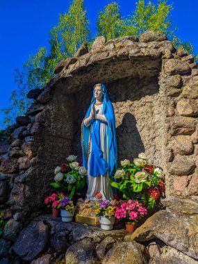 Mavi Bakire Meryem heykeli Kuzey Belarus 'taki Katolik hac alanında çiçeklerle süslenmiş taş mağarada duruyor. Yüksek kalite fotoğraf.