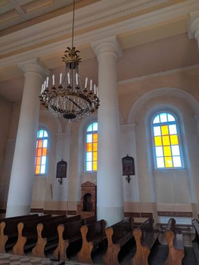 Volkovysk, Belarus, 1 Mayıs 2025. Geniş Katolik kilisesinin içi kareli mermer zemin beyaz sütunlar renkli cam pencereler ve süslü barok sunak resmi bir atmosfer yaratıyor. Yüksek kalite fotoğraf