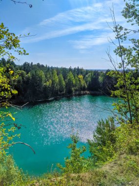 Volkovysk, Belarus, 1 Mayıs 2025. Çarpıcı turkuaz, yoğun yeşil orman ve parlak mavi bahar gökyüzünün altındaki beyaz kireçtaşı kayalıklarıyla çevrili tebeşirle taş ocağını taşırdı. Yüksek kalite fotoğraf