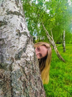 Brest, Belarus, May 01, 2025. Woman in mustard sweater embracing birch tree trunk showing emotional connection with nature among spring forest greenery. High quality photograph