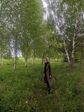 Novorudok, Belarus, May 01, 2025. Contemplative woman standing quietly among bright green birch forest enjoying peaceful spring nature atmosphere in woodland. High quality photograph