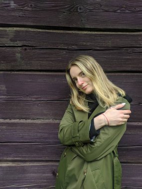 Novorudok, Belarus, May 01, 2025. Blonde woman in olive jacket sitting thoughtfully on dark wooden bench against rustic wall creating intimate portrait moment. High quality photograph