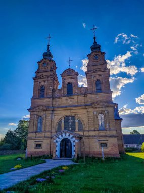 Novorudok, Belarus, 1 Mayıs 2025. Tarihi barok Katolik kilisesi, kumtaşı ön cepheli ikiz çan kuleleri ve klasik girişi parçalı bulutlu bahar gökyüzü altında. Yüksek kalite fotoğraf