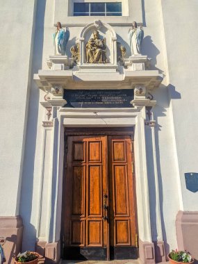 Dyatlovo, Belarus, 1 Mayıs 2025. Klasik mimari kompozisyonun üzerinde ahşap çift kapılı ve dini heykel oyuğu olan zarif beyaz barok kilise giriş kapısı. Yüksek kalite fotoğraf