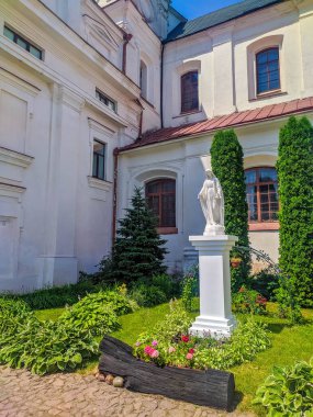 Minsk, Belarus, May 01, 2025. White classical church building entrance with columns and ornamental architectural details surrounded by lush green vegetation in spring season. High quality photograph