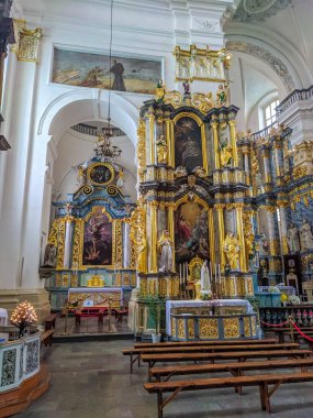 Grodno, Belarus, May 01, 2025. White baroque side altar with golden decorative elements and religious painting surrounded by arched architectural features in Catholic church. High quality photograph