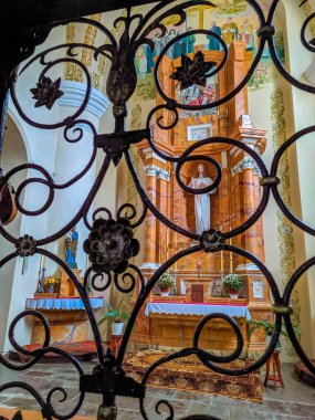 Grodno, Belarus, May 01, 2025. Decorative wrought iron gate detail with colorful floral ornaments featuring orange blue and gold painted scrollwork against white church interior wall. High quality photograph