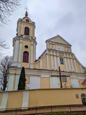 Grodno, Belarus, May 01, 2025. Yellow baroque church building with detached octagonal bell tower featuring arched windows and religious architecture under overcast spring sky. High quality photograph