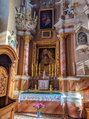 Lida, Belarus, May 01, 2025. Golden baroque altar with ornate religious decorations white candles blue cloth and statue of Virgin Mary in traditional Catholic church interior setting. High quality photograph