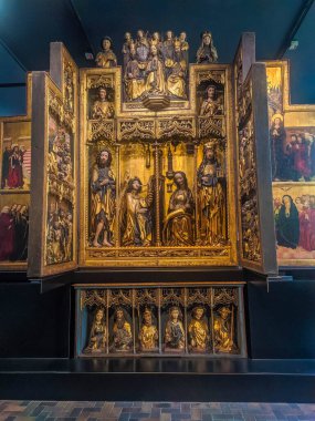 Warsaw, Poland, May 01, 2025. Illuminated golden medieval altarpiece with intricate carved panels displayed in dark museum gallery at National Museum Warsaw. High quality photograph