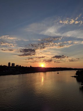 Gdansk, Poland, May 01, 2025. Spectacular golden sunset over Gdansk harbor with dramatic cloud formations and city skyline silhouette reflected in calm waters. High quality photograph