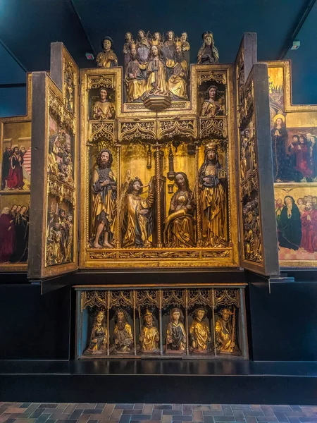 Warsaw, Poland, May 01, 2025. Illuminated golden medieval altarpiece with intricate carved panels displayed in dark museum gallery at National Museum Warsaw. High quality photograph