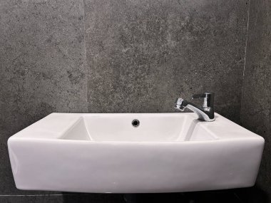 Modern duvara monte edilmiş beyaz seramik banyo lavabosu krom musluğu koyu gri fayanslı duvarlara monte edilmiş..