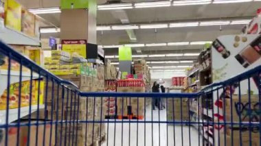 Bekasi, Endonezya - 25 Ocak 2026: İnsanlar bir süpermarket koridoru boyunca bir alışveriş arabasıyla dolaşırken rafları karıştırıyor ve satın almak için eşya seçiyorlar.