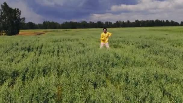 Flyger över en man i en gul jacka som dansar hip-hop i mitten av ett grönt fält — Stockvideo