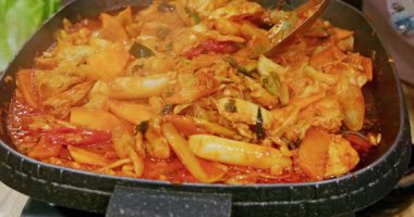 Demir bir tabakta Kore usulü baharatlı kızarmış bahar tavuğu pişirme işlemi karıştırılmış taze tavuk eti, çiğnenmiş pirinç keki ve parlak kırmızı baharatlı soslu kimchi içerir..