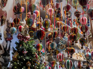 Renkli asılı balon şekilli süslemeler, şenlikli dekorasyonlar, heykelcikler ve küçük Noel ağaçlarıyla dolu kalabalık bir mağaza fotoğrafı. Neşeli detaylarla dolu parlak, canlı bir tatil pazarı sahnesi