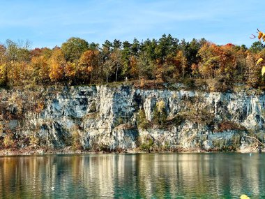 Zalew Zakrowek, Krakow, Polonya, sakin yeşil suların üzerindeki dikey kireçtaşı kayalıklarını gösteriyor, renkli sonbahar ağaçlarıyla kaplı ve dalgalı yüzeyde berrak mavi bir gökyüzünün altında yansıyor..
