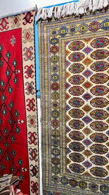 Geometrik ve çiçek desenli kırmızı, bej ve mavi tonlarda iki geleneksel doğu halısının yan yana asılması. Parlak, renkli ve dokulu kompozisyon..