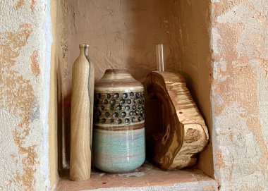 Üç dekoratif objenin yatay bir duvar desenli alçı, sıcak kum tonları, ahşap vazo, seramik kap ve ahşap blokla doğal bir görünüm oluşturan üç dekoratif fotoğrafı..