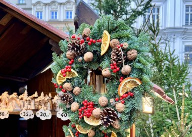 Polonya 'daki bir festivalde ahşap pazarda asılı duran yeşil kozalaklı, cevizli, kırmızı böğürtlenli ve kurutulmuş portakal dilimli Noel çelengi..