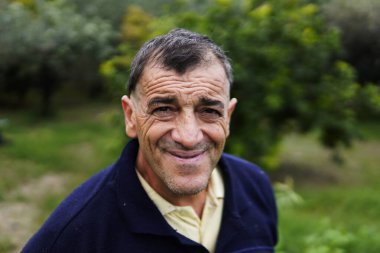 Neşeli orta yaşlı bir adam gülümseyip poz veriyor. Bu adam samimi ve doğal portrelerle neşe ve dostluk gösteriyor..