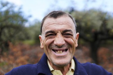 Neşeli orta yaşlı bir adam gülümseyip poz veriyor. Bu adam samimi ve doğal portrelerle neşe ve dostluk gösteriyor..