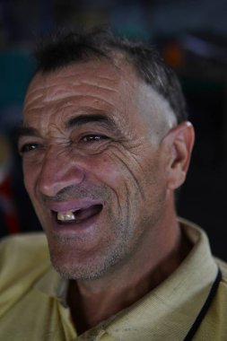 Neşeli orta yaşlı bir adam gülümseyip poz veriyor. Bu adam samimi ve doğal portrelerle neşe ve dostluk gösteriyor..