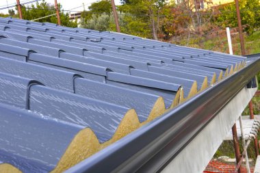 Çatı sandviç panelleri. Yalıtımlı metal sandviç panelleri kuruluyor. Kiremit desenli antrakit gri metal çatı kaplamalarının üst görüntüsü. EPDM ile sürgüler.