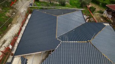 Karmaşık bir binaya antrasit metal çatı kiremitleri yerleştirilmiş. Yüksek açılı İHA görüntüleri, inşaatın inşaat alanındaki ilerlemesini gösteriyor. Yenilikçi yalıtım malzemeleri.