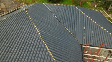 Karmaşık bir binaya antrasit metal çatı kiremitleri yerleştirilmiş. Yüksek açılı İHA görüntüleri, inşaatın inşaat alanındaki ilerlemesini gösteriyor. Yenilikçi yalıtım malzemeleri.
