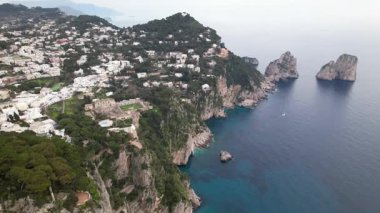 Capri kasabası, Faraglioni şehri ve manastır. Capri kasabasının beyaz mimarisini, San Giovanni Manastırı 'nı ve Faraglioni' nin kayalarını gösteren geniş bir hava manzarası.