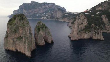 Capri, İtalya açıklarındaki Faraglioni kaya oluşumlarının hava görüntüsü. İkonik Faraglioni kireçtaşı kayalıklarının sinematik görüntüleri. Video Faraglioni di Mezzo 'nun doğal kemerini yakalıyor..
